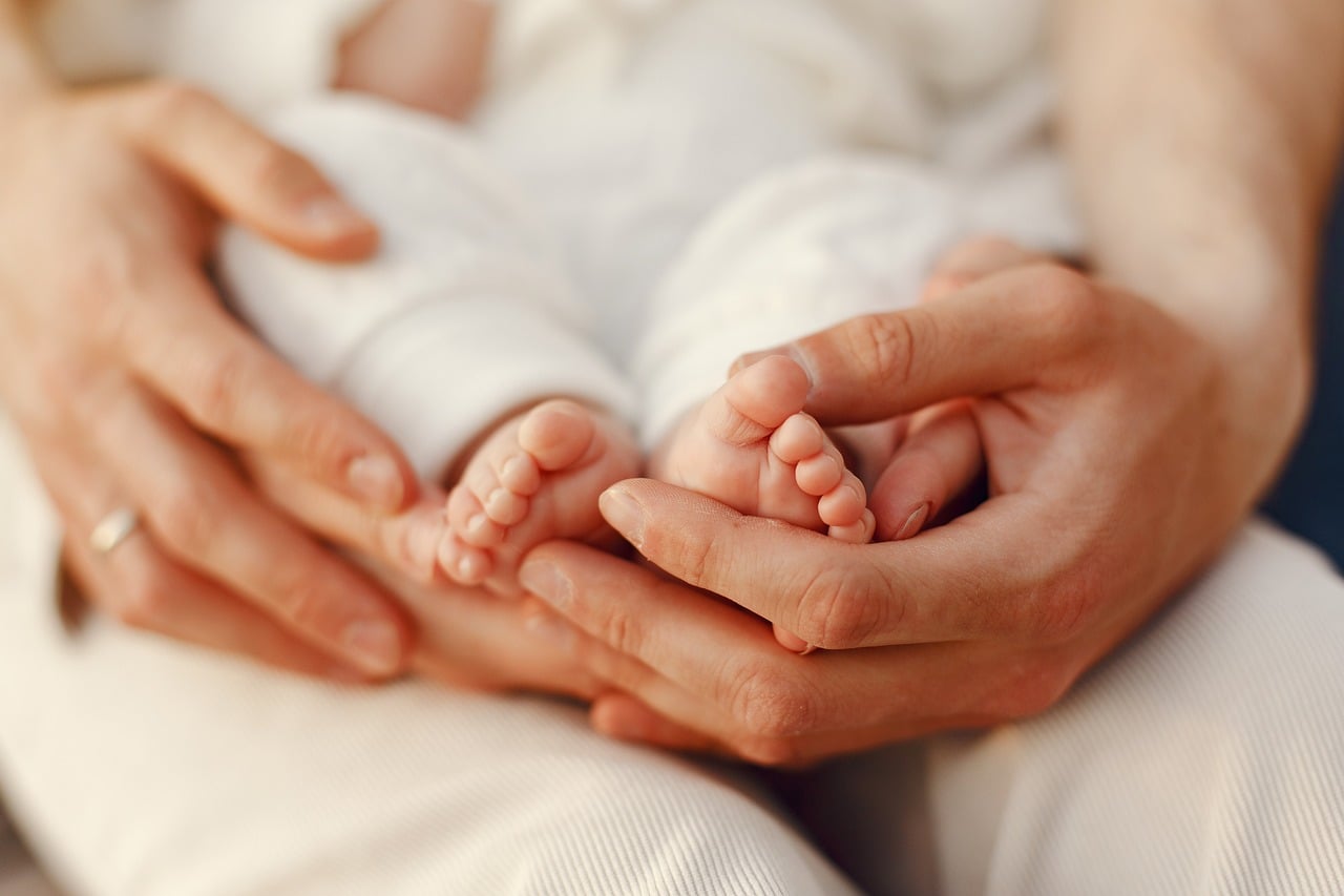A parent's hands gently cradling a newborn baby's foot